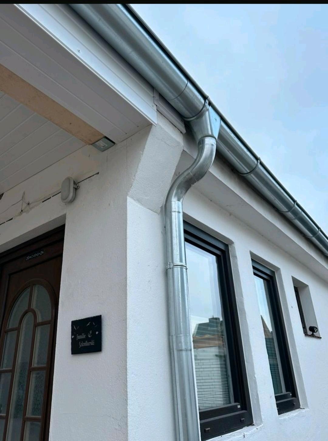 Neue Zinkdachrinne mit Fallrohr und Bogen an einem verputzten Wohnhaus